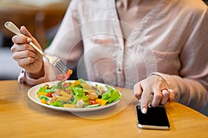 Calories counting and food control concept. Woman using smartphone with black screen and eating fresh salad