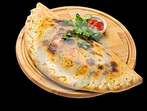 Calzone pizza on a round wooden board isolated on black background. photo