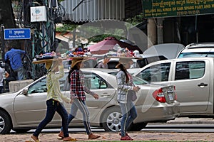 Cambodian females street vendor put the threshing basket of cosmetics and accessories for women on her head and walking for sell