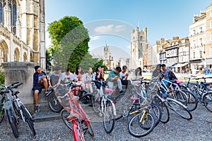 Many people seat in shade near gothic King`s College Porters` Lodge, many bikes