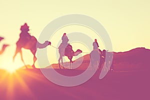 Camel caravan with people going through the sand dunes in the Sahara Desert. Morocco, Africa