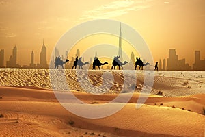 Camel caravan on sand dunes on Arabian dessert with Dubai skyline at sunset