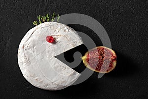 Camembert or brie cheese like pacman eating fig fruit on black background. Creative food concept