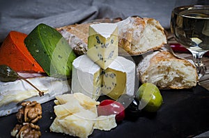 Mix cheese on dark background on wood board with grapes, honey, nuts, tomatoes and basil. Top view