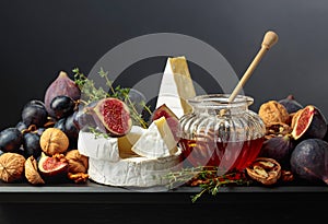 Camembert cheese with fruits and honey on a black background