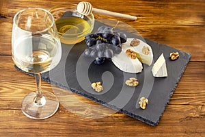Camembert cheese, nuts, honey and sweet grapes on the background of a glass of white dry wine