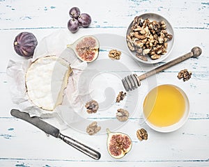 Camembert cheese on old wooden table with a bowl of walnuts, honey, a vintage table knife, cut figs grapes, top view