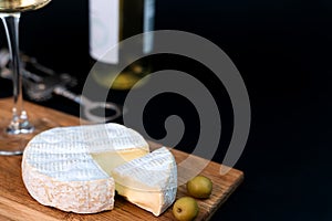 Camembert cheese, olives and wineglass of white wine on a dark background. Close-up. Copy space. Selective focus