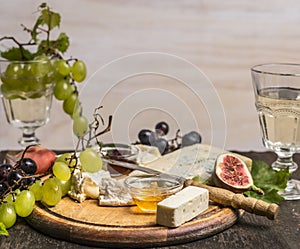 Camembert, Dor Blue, Gorgonzola, honey, grapes and wine on a cutting board wooden rustic background top view close up