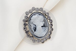 Cameo brooch, which is a side portrait of a woman, with small crystals around the edges on a white background.