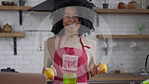 Camera approaches to young smiling African American woman juggling oranges posing in kitchen at home. Portrait of