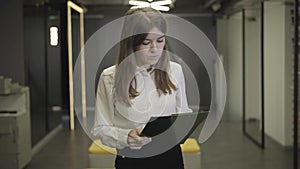 Camera approaching thoughtful Caucasian young woman looking at documents in open space office. Portrait of pretty
