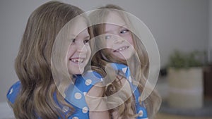 Camera approaching to faces of two identical twin sisters talking and laughing. Brunette cheerful girls in blue dotted