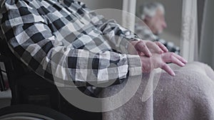 Camera approaching to unrecognizable man`s hands shaking. Elderly disabled man sitting in wheelchair and reflecting in