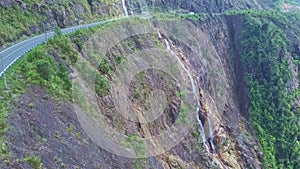 Camera Flies along Highway on Steep Cliff and Waterfall