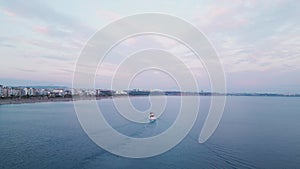 The camera flies behind a yacht sailing on open water towards a city at sunset.