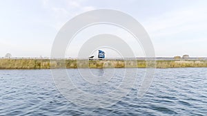 Camera flying along the rippled river with a driving truck on the background. Scene. Aerial view of a lorry driving