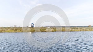 Camera flying along the rippled river with a driving truck on the background. Scene. Aerial view of a lorry driving