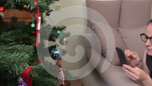 Camera focusing on Christmas decoration on Christmas tree then on woman who relaxing on sofa