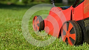 Camera following lawn-mower mowing lawn in courtyard. Close up. An electric lawn mower machine mows green grass in
