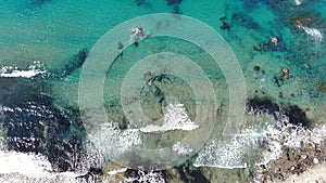 Camera following turquoise foamy waves rolling on sandy beach with pebbles. Aerial view of gorgeous Mediterranean Sea