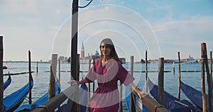 Camera follows beautiful happy brunette Caucasian tourist woman walk on famous gondola pier in Venice on summer trip.