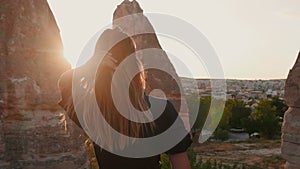 Camera follows beautiful young woman running in slowmo in beautiful bright sunset light with views of Cappadocia, Turkey