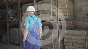 Camera follows confident Caucasian man walking on manufacturing site storage facilities. Adult male worker in uniform