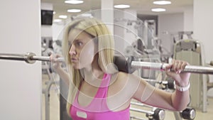 Camera follows movement of concentrated confident woman squatting with weights on shoulders. Portrait of beautiful blond