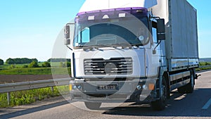 Camera follows to truck with cargo trailer driving on highway and transporting goods at summer day. Lorry riding through