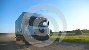 Camera follows to truck with cargo trailer driving on highway transporting goods at sunny day. White truck speeding