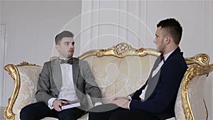 Camera goes down. Two handsome businessmen in suits sitting on a sofa discussing business.