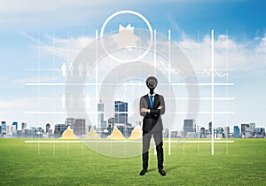 Camera headed man standing on green grass against modern cityscape