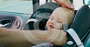 Camera inside the car Closeup baby boy sitting in the baby car seat inside of car Father's hands unfastening seat