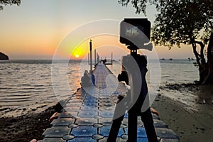 Camera mounted on a tripod photograph man and woman on the pier and sunrise