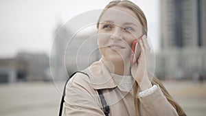 Camera moves around beautiful face of young charming Caucasian woman talking on smartphone. Close-up portrait of happy