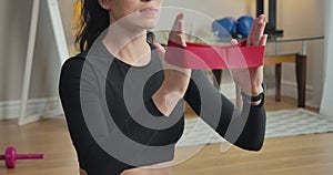 Camera moves down along slim body of young concentrated sportswoman training hands with resistance band. Young beautiful