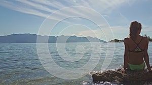 Camera Moves from Girl Sitting on Rock in Ocean to Hilly Beach