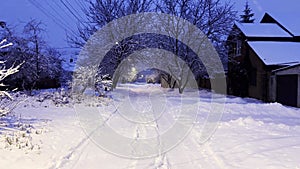 Camera moving along snowy country road at evening time. Street lamp illuminating snow trail at winter night. Beautiful