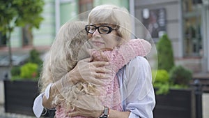 Camera moving around hugging grandmother and granddaughter. Happy smiling senior Caucasian woman in eyeglasses embracing