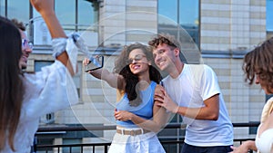 Camera moving back from happy young couple boyfriend and girlfriend taking selfie photos on smartphone outdoors at party