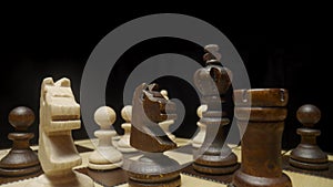 Camera pans over chessboard with chess pieces placed and focuses on brown horse. White and brown wooden chess set on