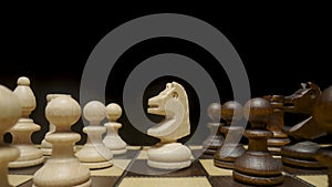 Camera pans over chessboard with chess pieces placed and focuses on white horse. White and brown wooden chess set on