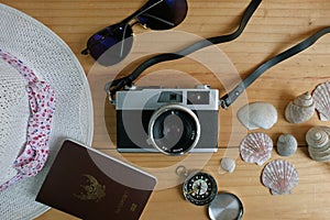 Camera, passport, sunglasses, hat, shells and message let`s go travel on wooden floor