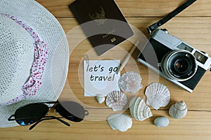 Camera, passport, sunglasses, hat, shells and message let`s go travel on wooden floor