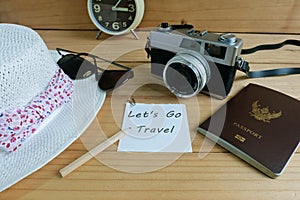 Camera, passport, sunglasses, hat, shells and message let`s go travel on wooden floor