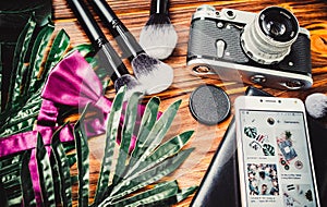 Camera, phone and makeup brushes on wooden brown background with green leaves