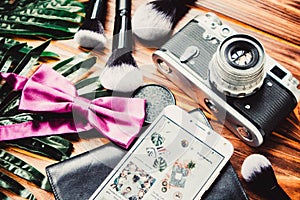 Camera, phone and makeup brushes on wooden brown background with green leaves