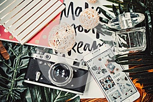 Camera, phone and perfume on wooden brown background with green leaves