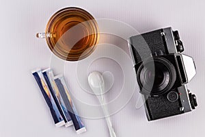 A camera, a photo reporter`s tool at the table a cup of morning strong tea, sugar, on a white background, a blank for design solut